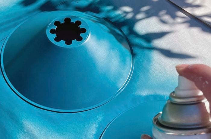 A person sprays a lampshade outdoors using spray paint.