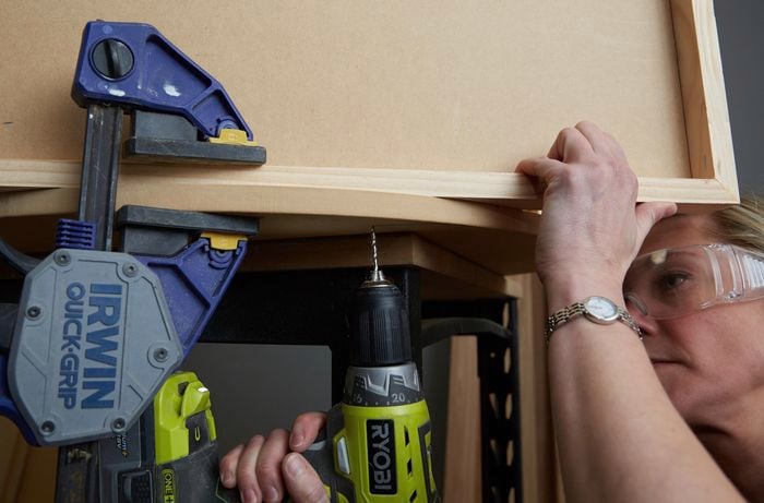 Pieces of timber clamped together while person drills nails in to them