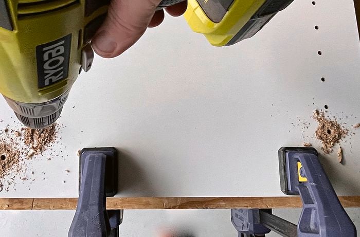 A person using a drill to create holes for cupboard shelving] 
