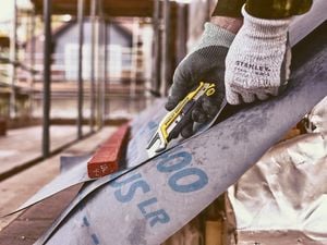 A person wearing gloves cuts building wrap with a utility knife at a construction site.