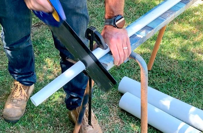 A person cutting PVC pipe with a saw.