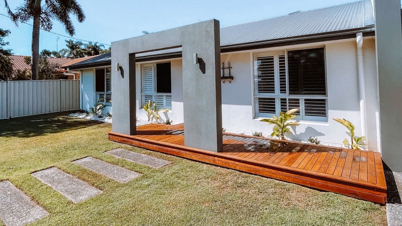 Exterior front of house, with white walls, grey roof and grey archway with a brown wood timber entrance deck across the front showcasing an outdoor decking solution.