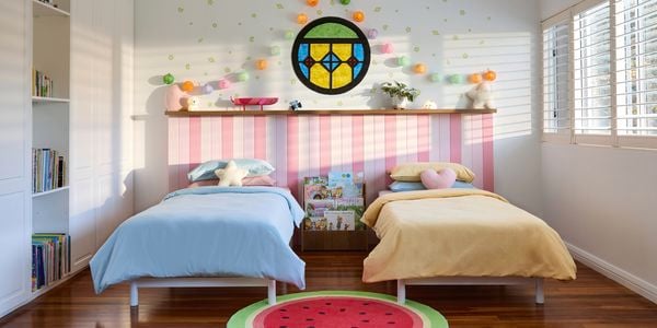 Two single beds in a Bluey-inspired bedroom with a watermelon rug, stained glass window, lanterns and pink bedhead panelling
