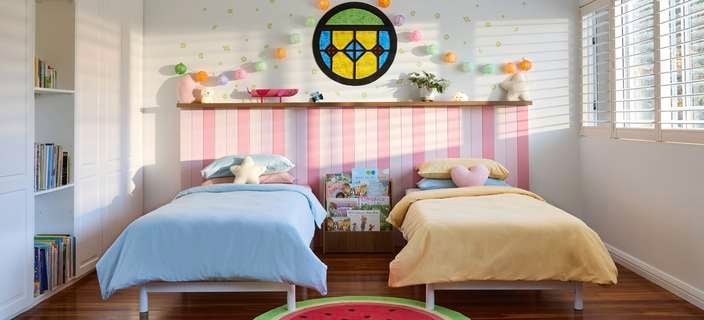 Two single beds in a Bluey-inspired bedroom with a watermelon rug, stained glass window, lanterns and pink bedhead panelling