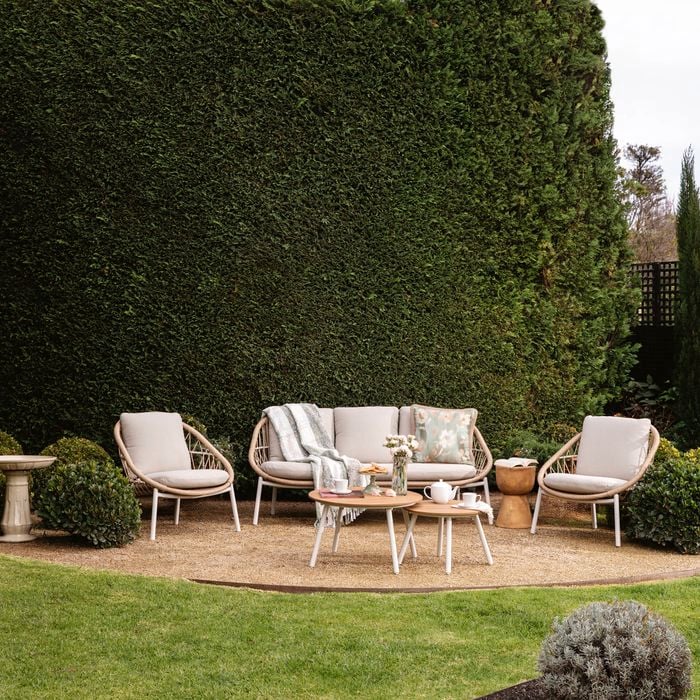 Cane outdoor setting outside on a paved area with hedging behind it.