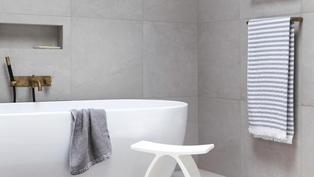 Freestanding bath with foliage in the background and grey bathroom tiles