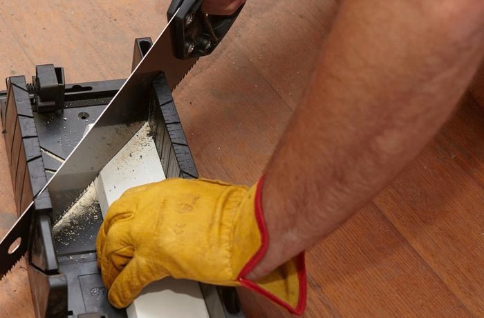 A person cutting architrave with a hand saw and mitre box