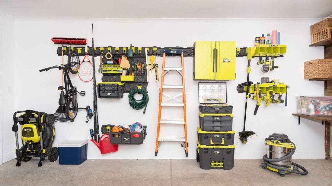An organised garage wall showcases the Ryobi LINK rail system neatly holding tools, storage bins, shelves, a ladder, a hose, and other equipment
