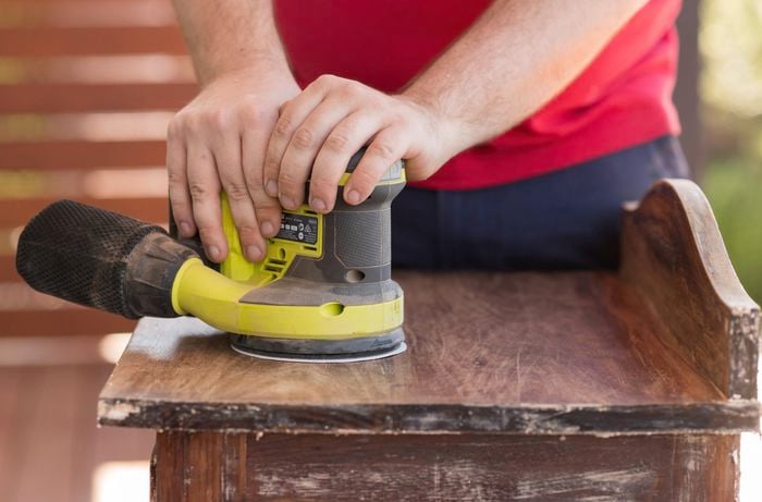 Sand the surface of a wooden cabinet using a Ryobi sander