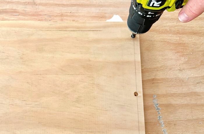 Hand drilling holes along edge of wood.