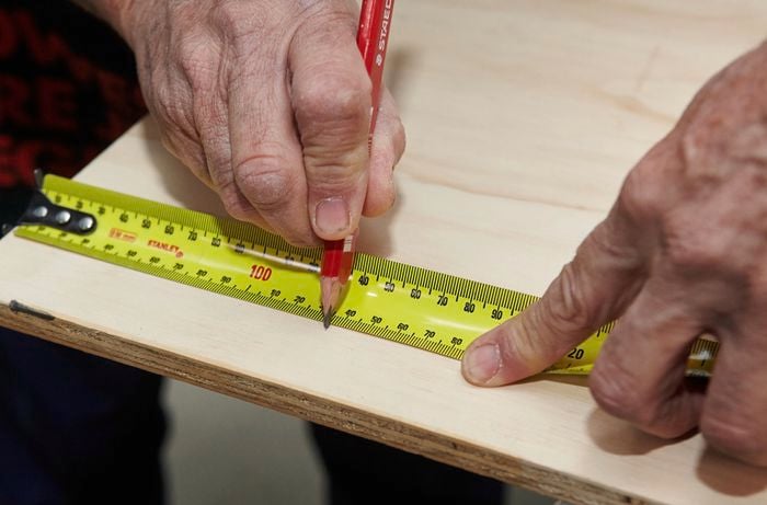 A person marking length on a timber panel using a measuring tape and pencil
