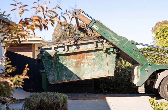 A green skip bin is being lifted onto a truck in a residential driveway.