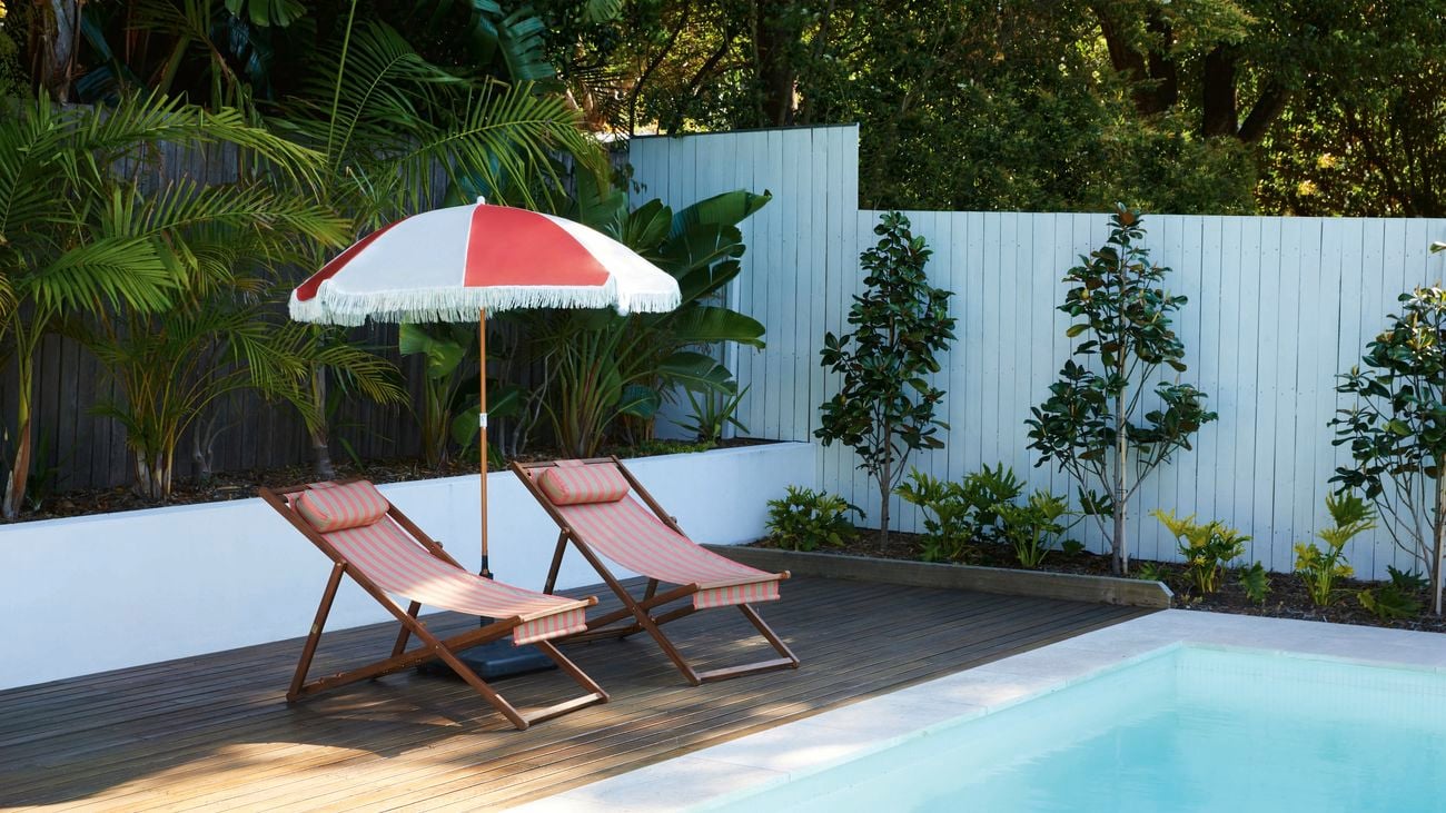A blue pool with two lounges and an orange and white umbrella.