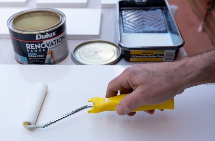 A person is applying a satin clear coat with a roller on a painted surface which will help protect against scratches, chips, and wear and tear