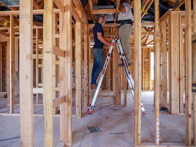Two people standing on either side of A-frame ladder