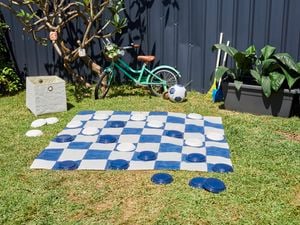 A large plastic checkers mat with and pieces on an area of grass next to a child's bicycle