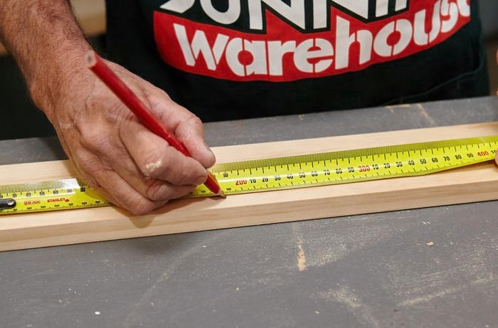 A person marking length on timber using a measuring tape and pencil