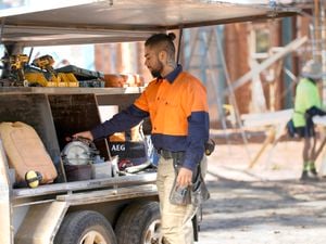 A tradie taking a saw out of a trailer on a work site.