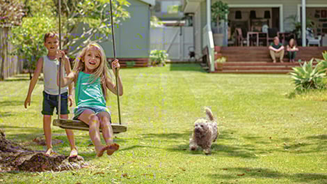 Children and a dog playing in the backyard while parents look on from a deck