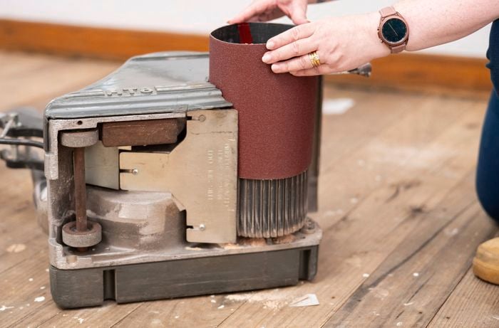 ​A close-up of a person fitting a sanding belt on a floor sanding machine to continue through finer sanding stages.
