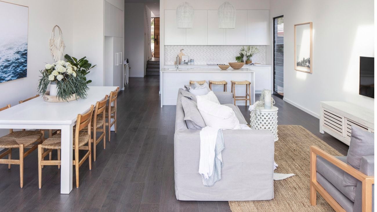 Coastal inspired furniture, white dining table, couch and TV set in a lounge interior.