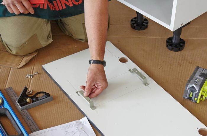 A person positioning brackets on the inside a cabinet panel