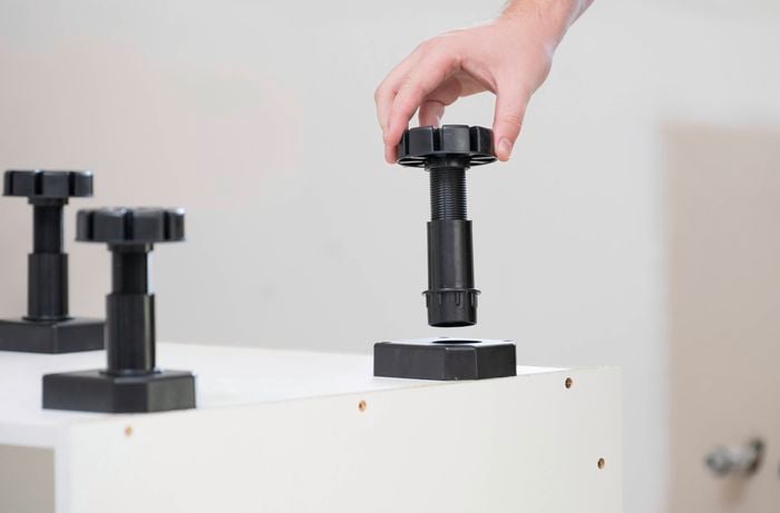 A person is attaching adjustable feet into the base of a cabinet.