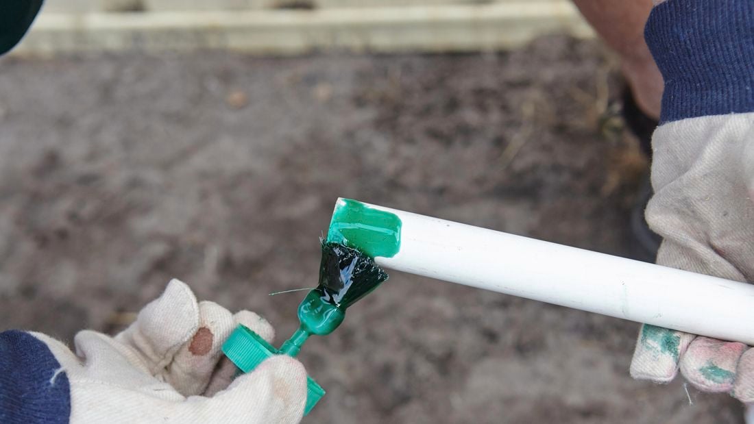 A person applying green adhesive to the end of a PVC pipe