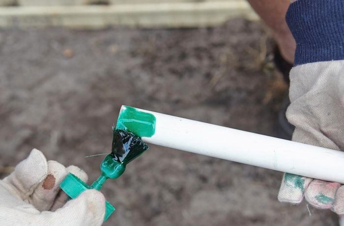 A person applying green adhesive to the end of a PVC pipe