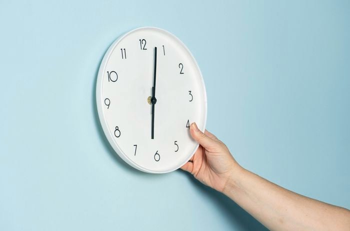 A person is holding a white wall clock against a light blue wall, preparing to upcycle it into a bold retro wall clock feature. 