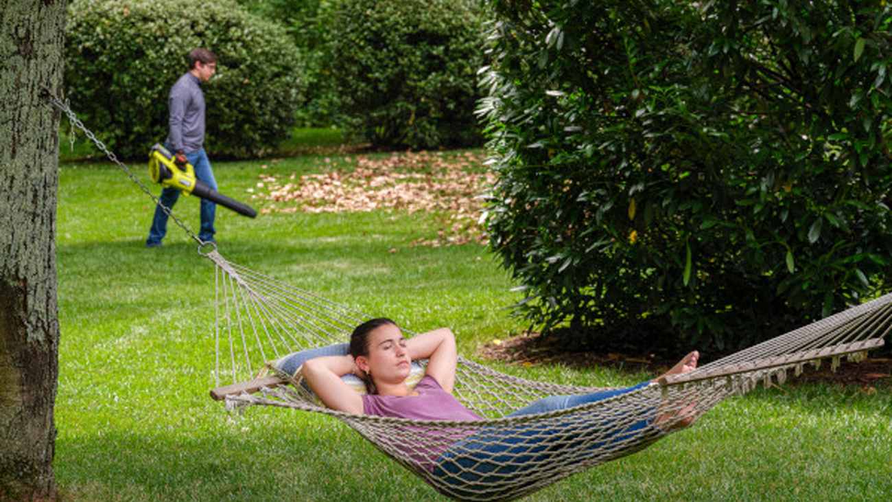 person laying in a hammock and person using a leaf blower in the back ground