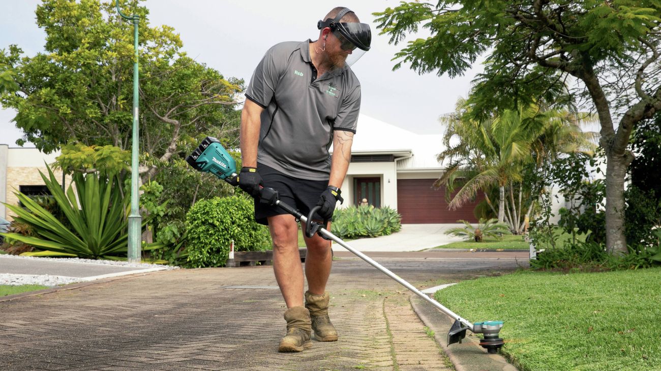 Person using a line trimmer to edge grass along a residential driveway.