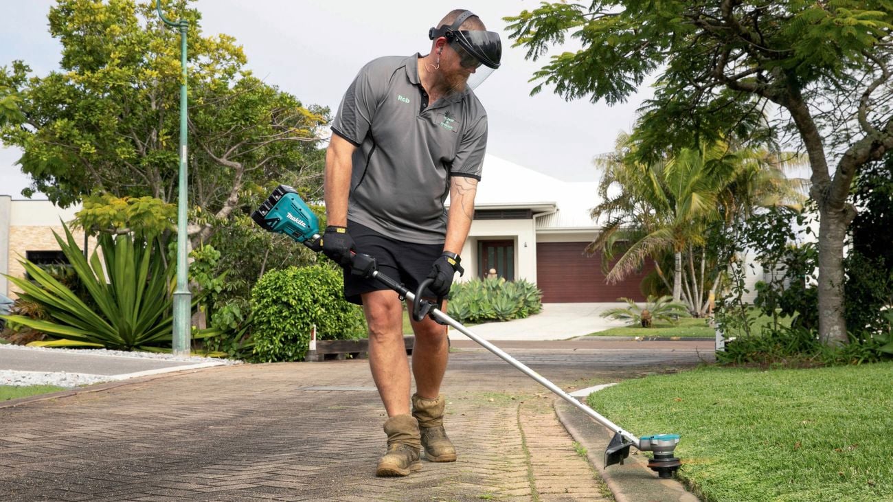 Person using a line trimmer to edge grass along a residential driveway.