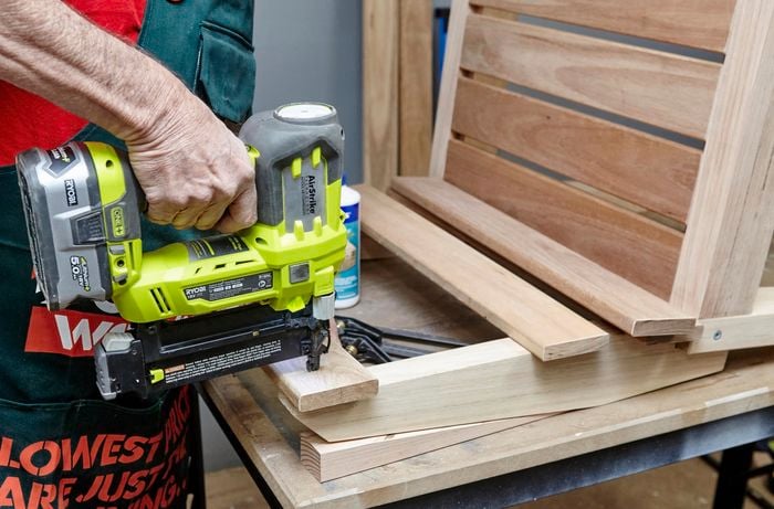 A wooden plank being nailed to a chair with a nail gun as part of a chair's backrest