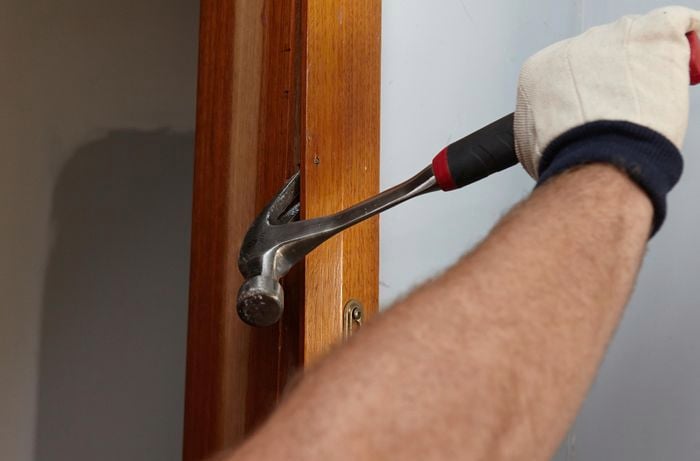 A door jamb being pried free from the wall with a claw hammer