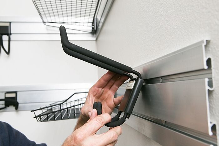 Close up of person slotting storage hooks into a wall mounted rail