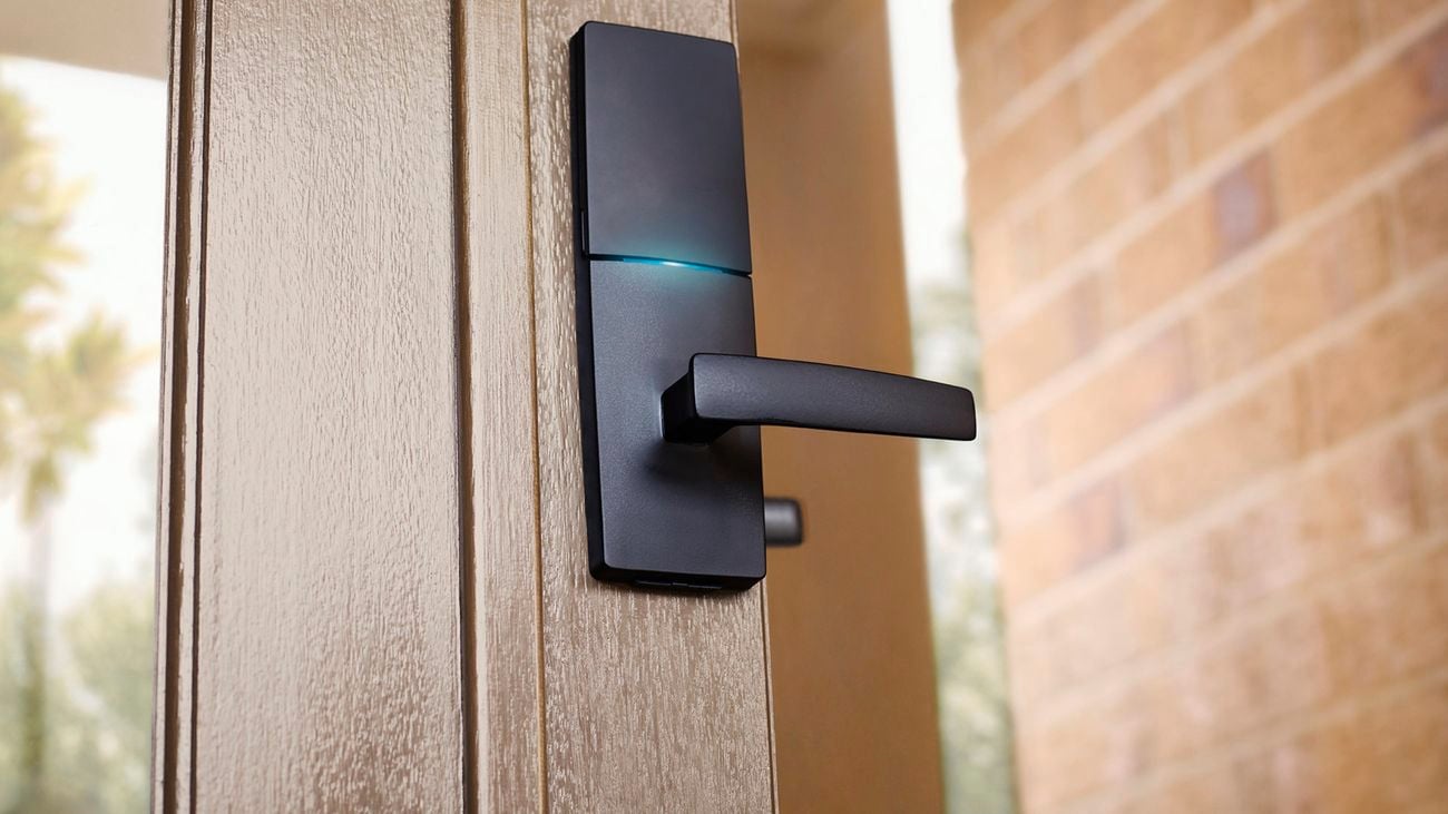 Close up of a black Gainsborough smart lock installed in a wooden-framed glass front door.