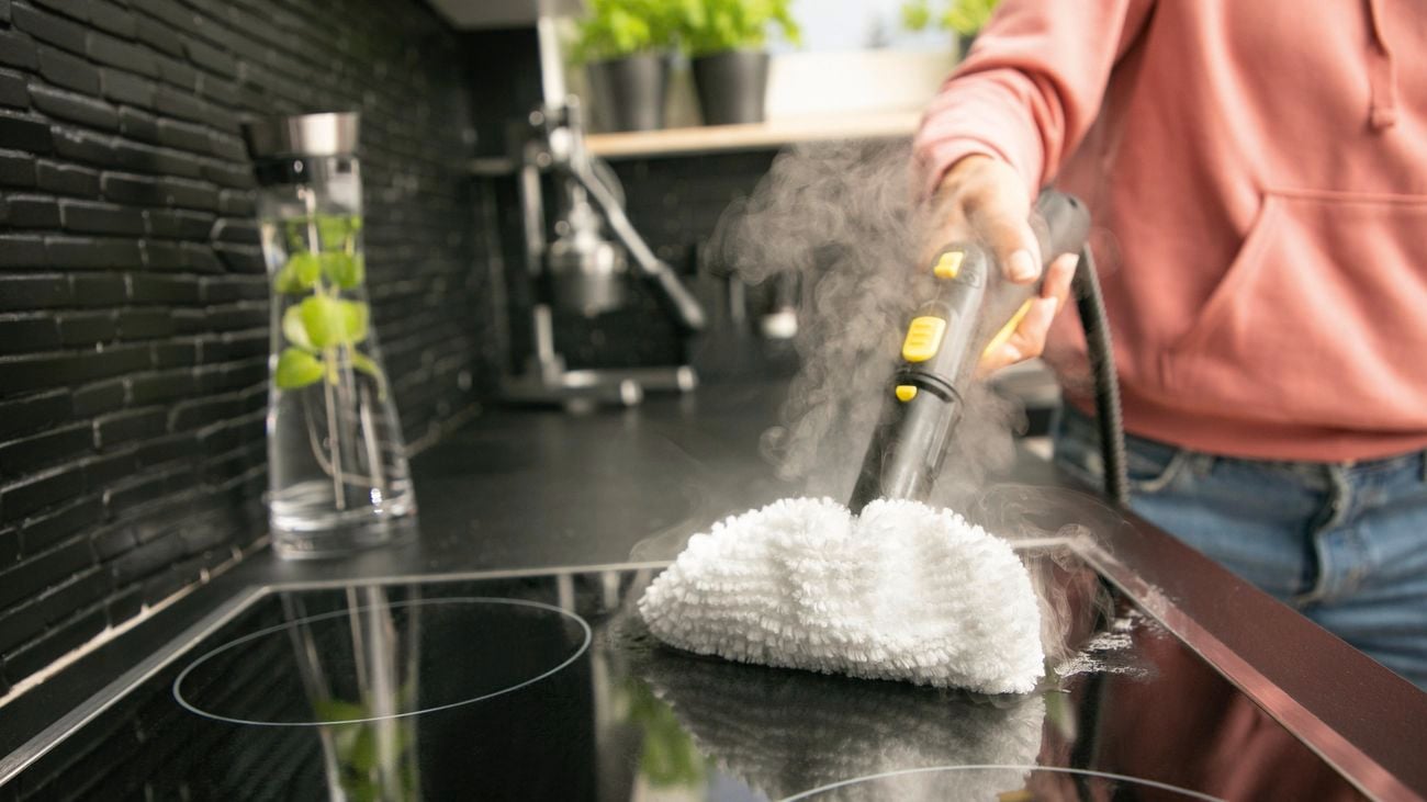 Person using handheld steamer to clean induction cooktop.
