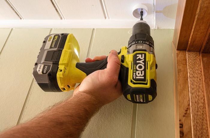 A person drilling the ceiling with a drilling machine.