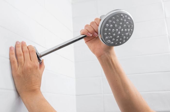 ​A person is removing an old shower head by turning it anti-clockwise, preparing the fitting for installation of a replacement shower head