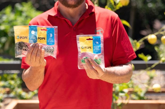 A Bunnings Team Member is holding two packs of jet spray irrigation fittings. 