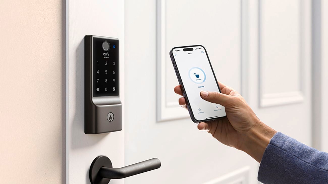 A hand using smartphone to connect the Eufy security app to the smart lock on the door.
