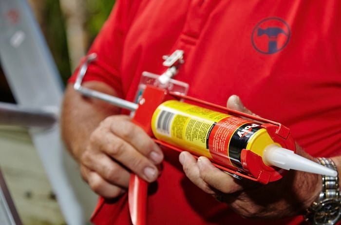 Person holding a caulking gun containing a tube of silicone