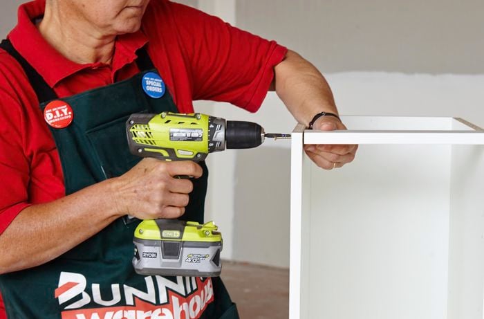 Person attaching cabinet rail using a drill
