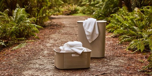 Ezy Storage Kora laundry basket and hamper with folded white towels on a garden pathway surrounded by ferns.