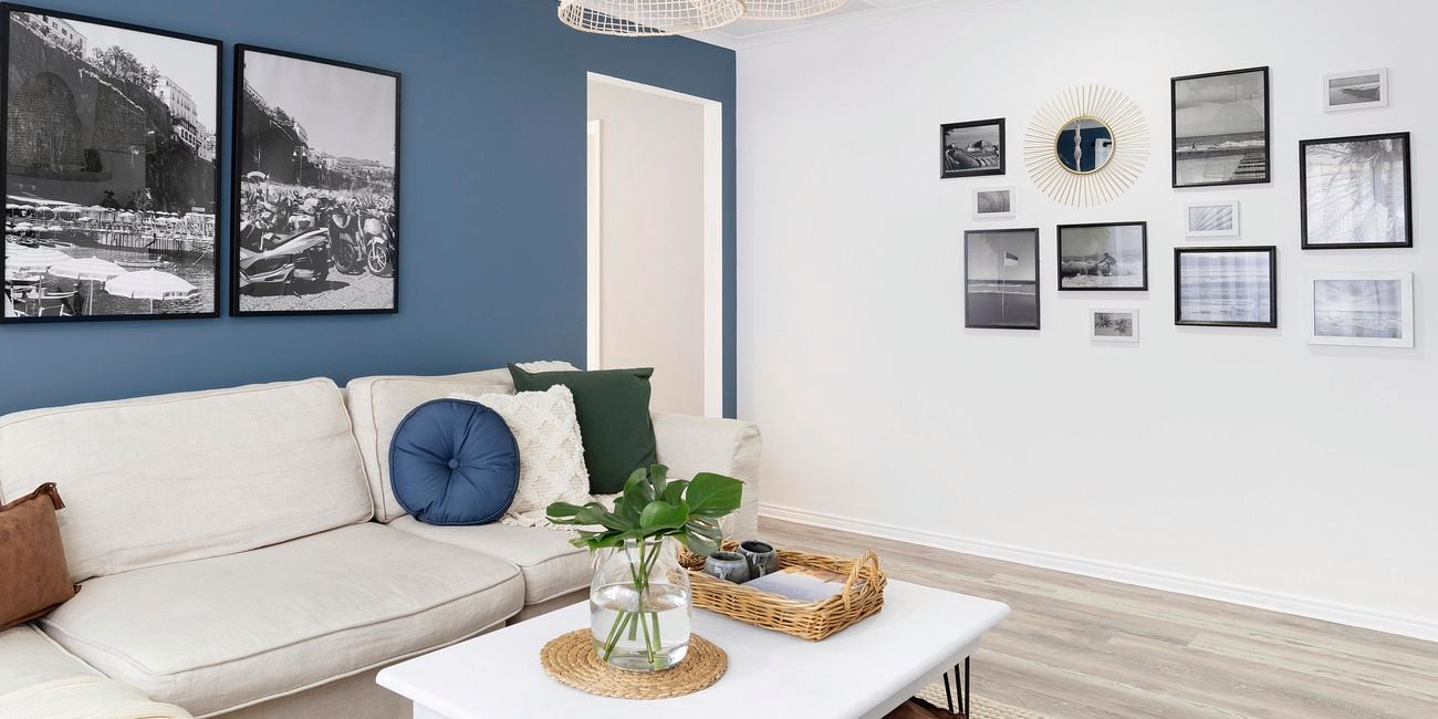 Living room with blue feature wall, white couch, white coffee table and pictures hanging on the wall.