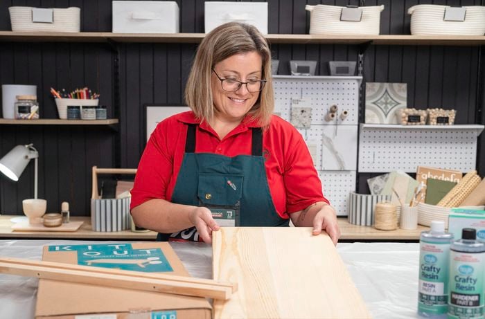 A woman is holding a plain wood panel.
