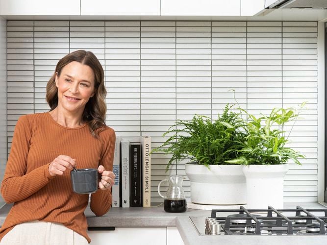 lady in kitchen with a hot drink, silver hot plates and assorted green ferns sitting on bench top