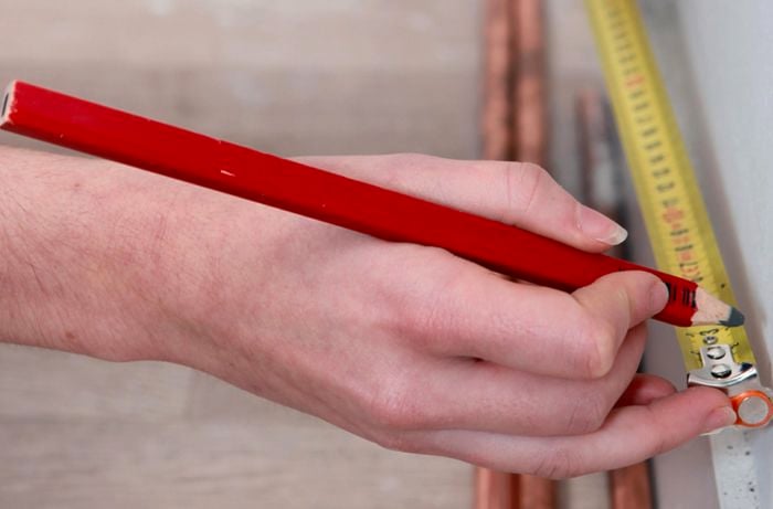 Close up of a person marking a spot with a pencil against a measuring tape
