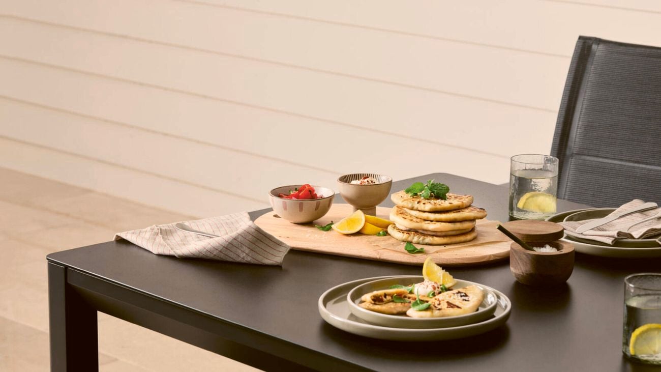 A stack of Turkish gozleme on a wooden board with lemon wedges, and a plate with a single gozleme garnished with mint and yoghurt